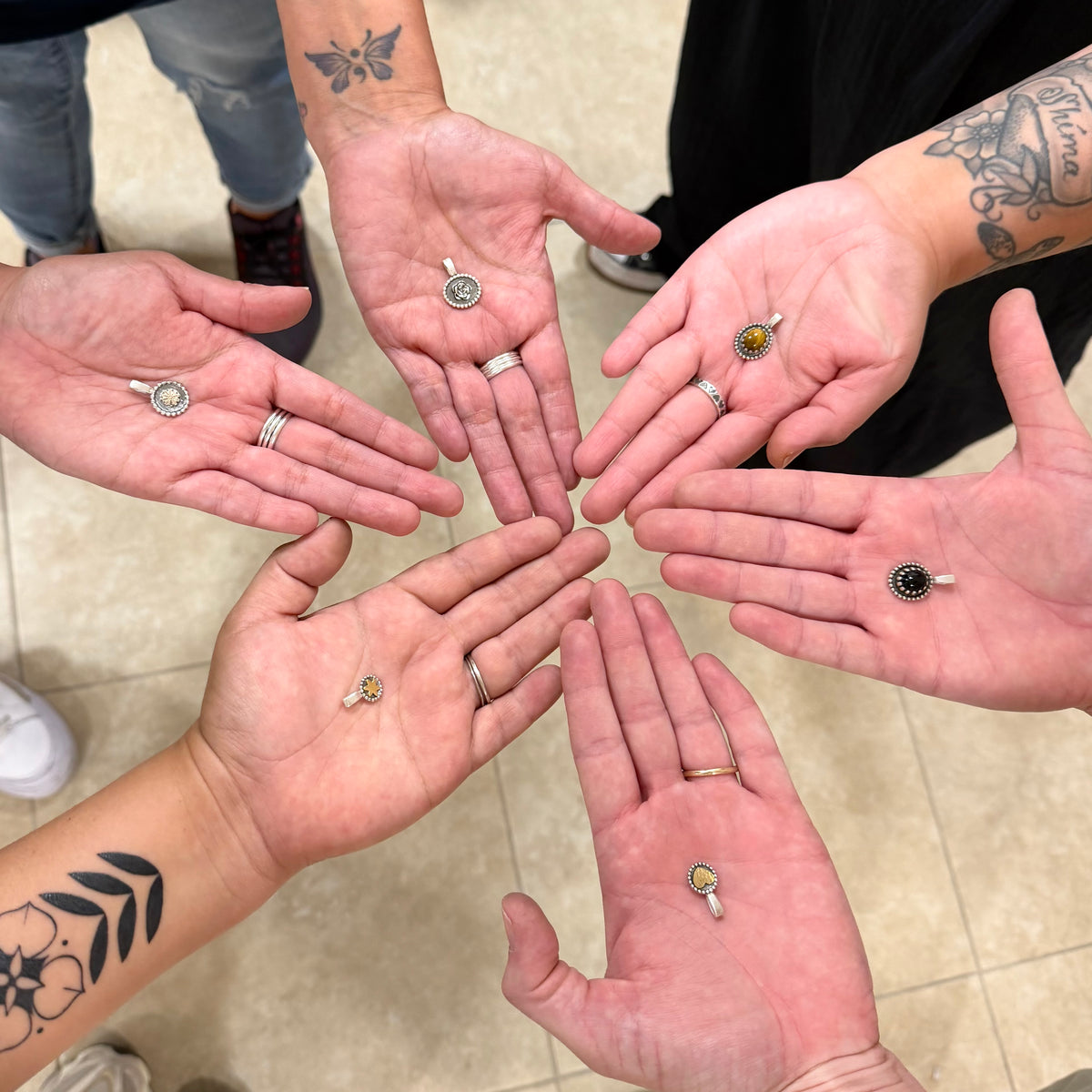 Hands with various rings held out in a circle, showing off jewelry.